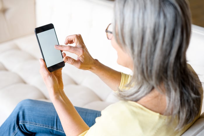 Woman holding smartphone in both hands, focused on screen, casual indoor setting, modern communication