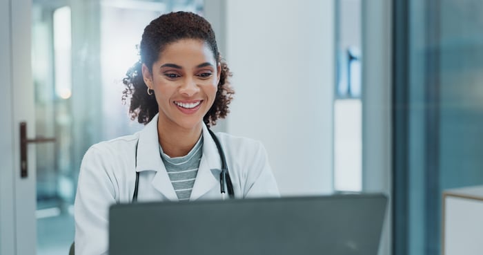 Female doctor smiling at her computer while using a digital health system
