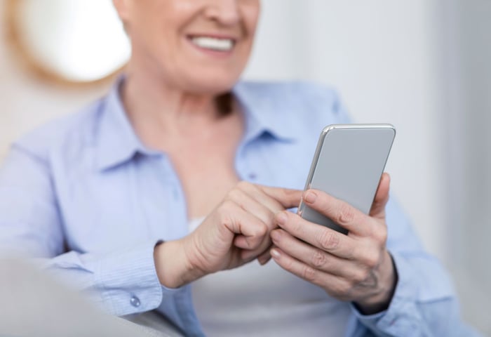 A woman holding a smartphone, looking at the screen, using a mobile app in a comfortable setting