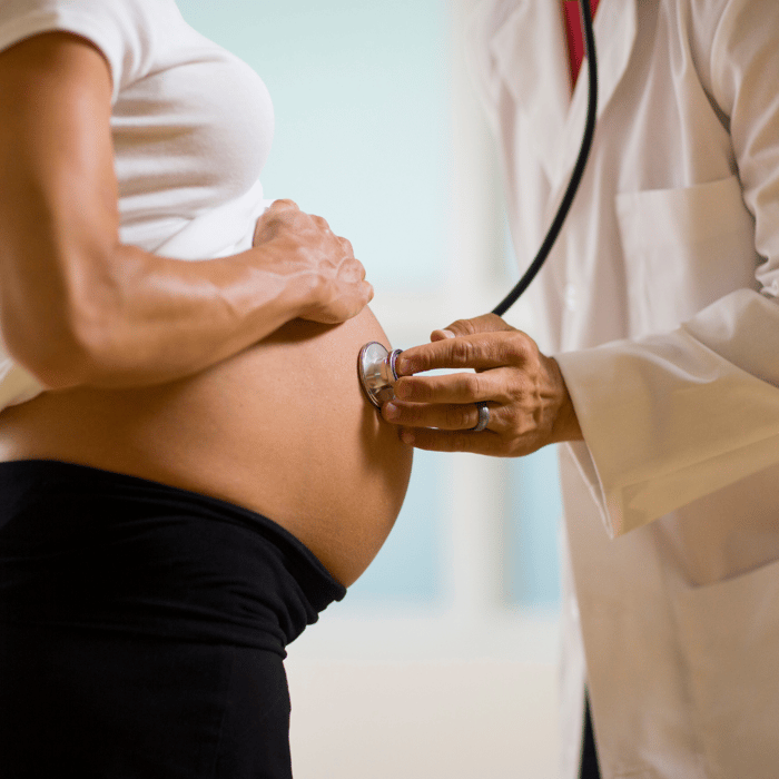 Doctor examining a pregnant woman’s belly, illustrating remote guidance, patient education, and clinical support in maternity.